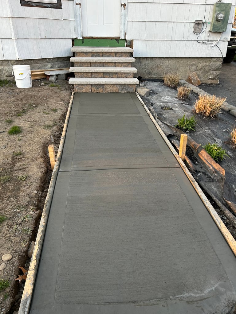 Concrete walkway leading to mobile home entrance with stone steps and wooden border edging