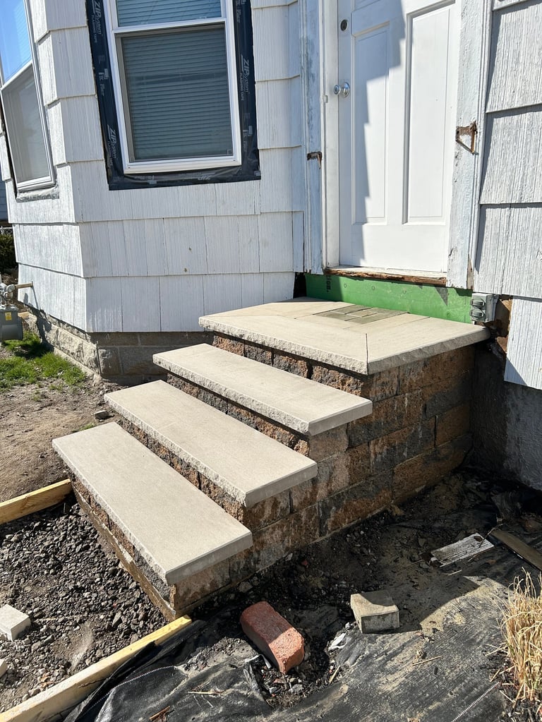 Concrete steps leading to a white mobile home entrance with a brick foundation and green artificial turf