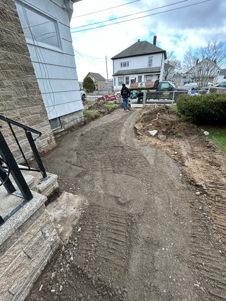 Residential construction site with dirt pathway between houses, workers visible, and clear sky